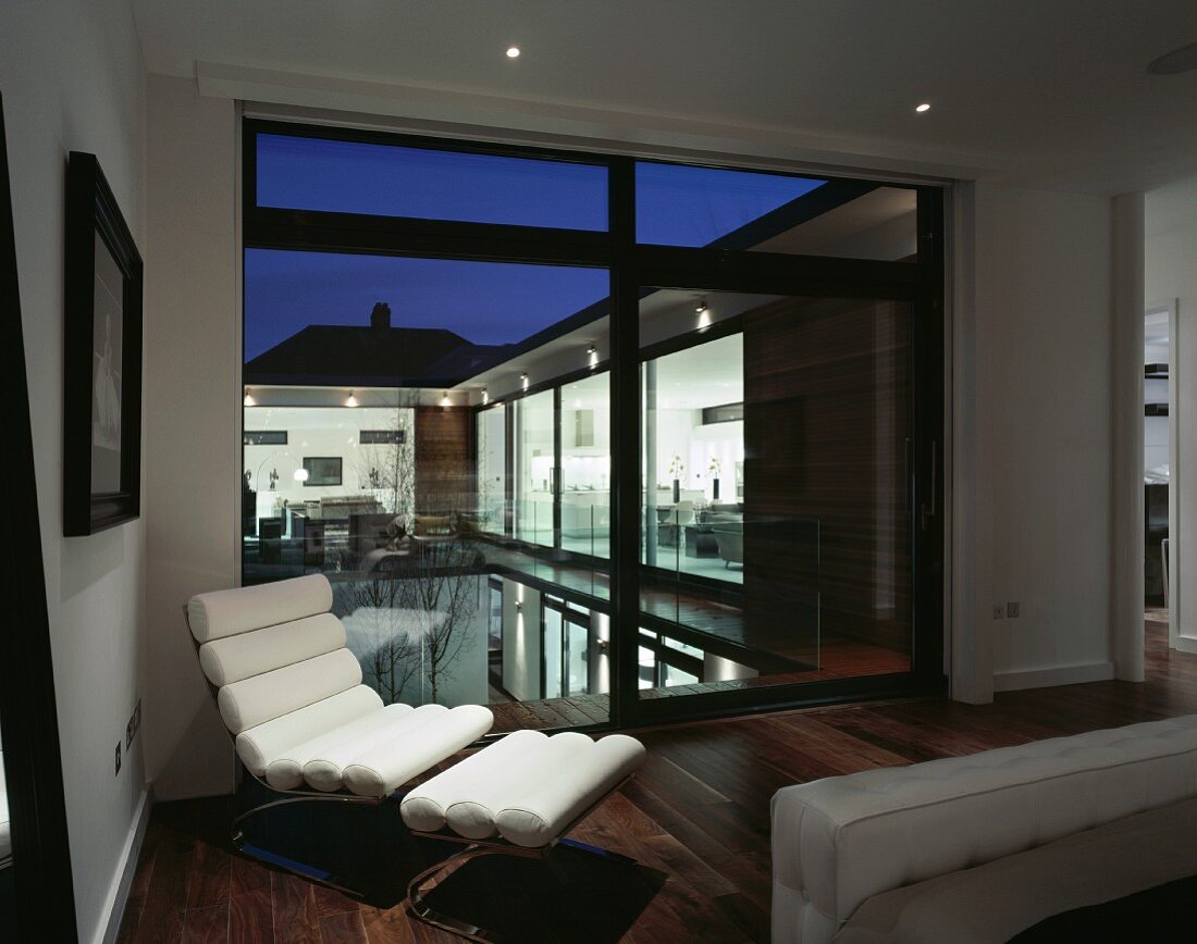 Moderne weiße Lederliege mit Fussablage vor Terrassenfenster und Blick auf Pool in Abendstimmung