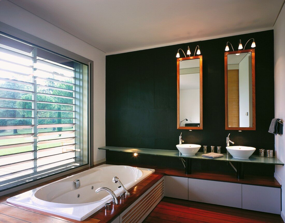 Designer bathroom with the tub built into a platform in front of a window and vanity on a dark wall