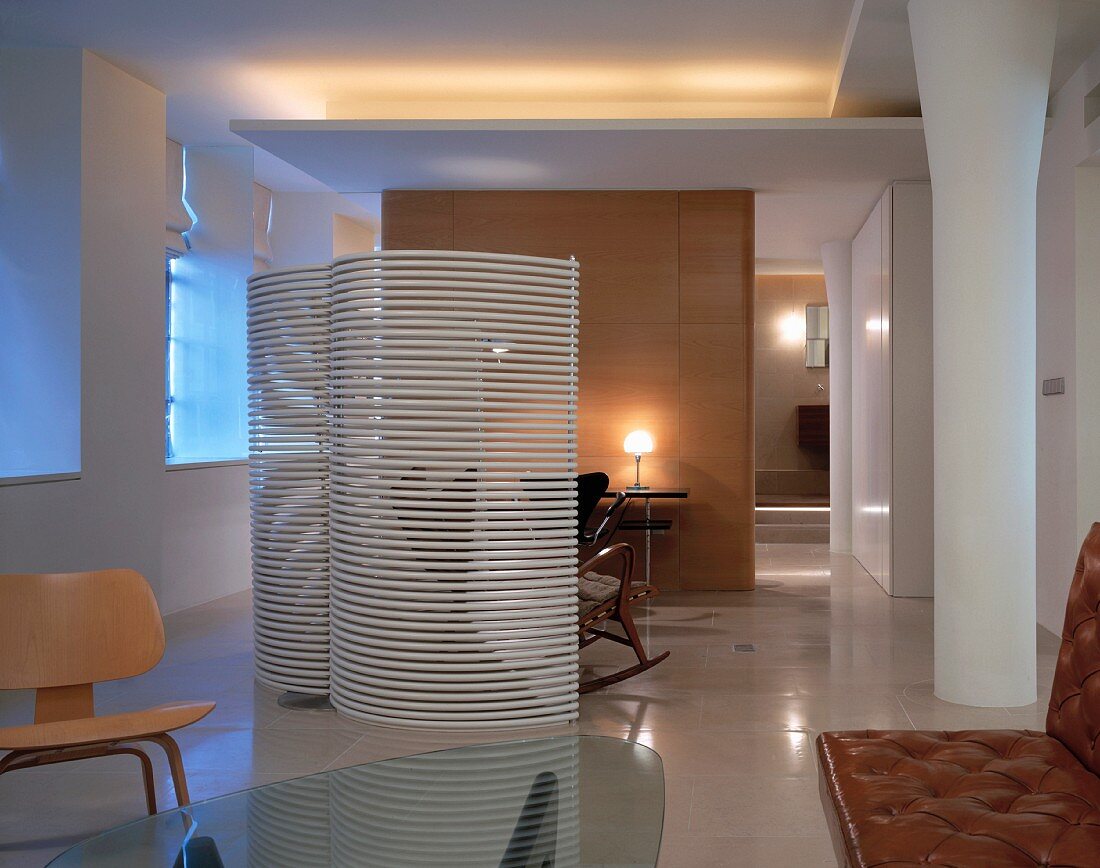Moderner Wohnraum mit gebogenem Paravent aus weissen Lamellen und verschiedenen Sitzmöbeln im Bauhausstil