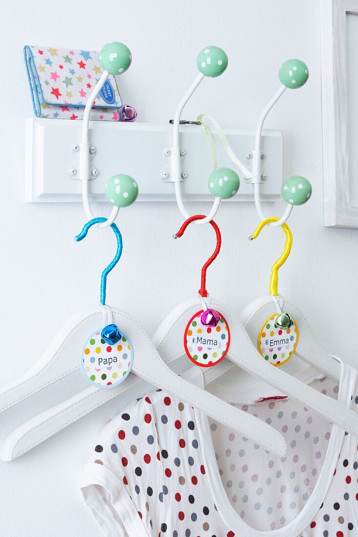 Coat hangers decorated with buttons, ribbon and name tags hanging on a wall mounted coat rack