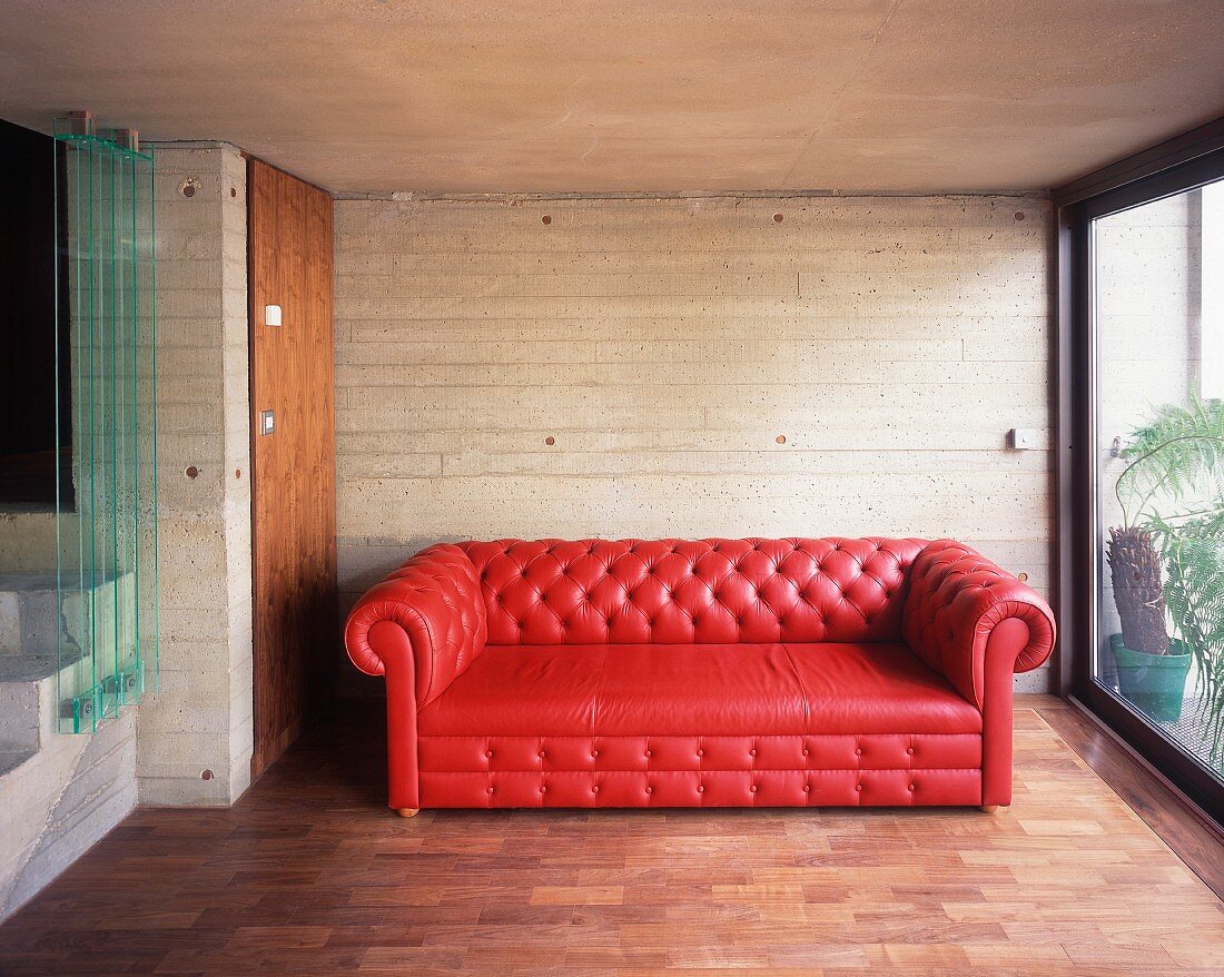 Brick-red leather sofa in front of a concrete wall next to a terrace window
