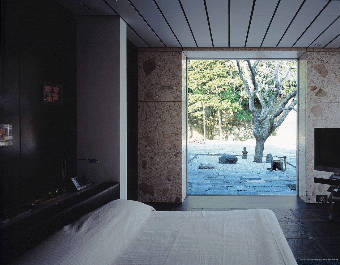 Schlafzimmer mit offener Terrassentür und Blick auf knorrigen Baum im gestalteten Innenhof
