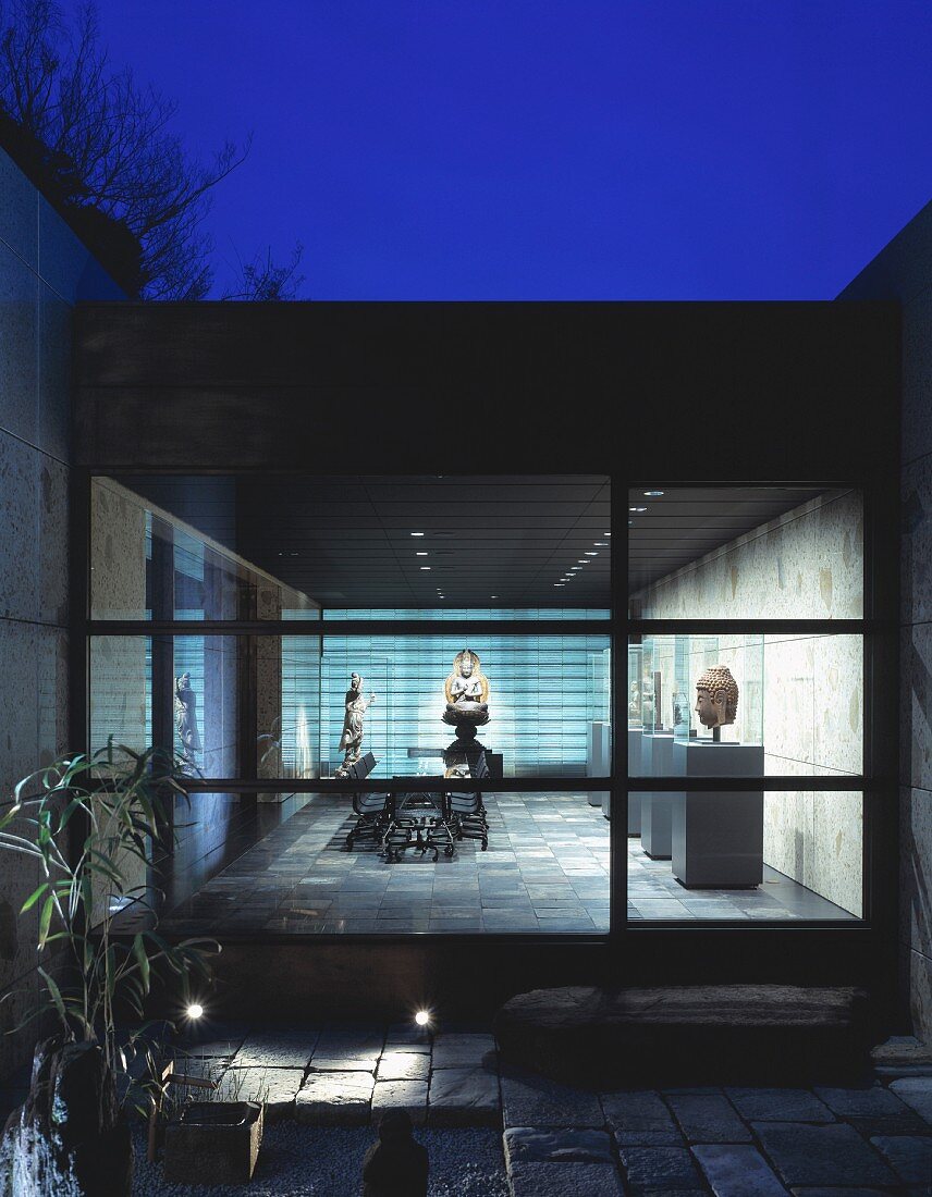 Modern, Japanese home in the evening light with a view through a terrace window into an illuminated exhibition space