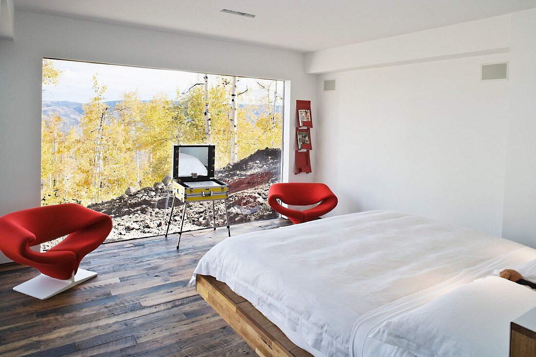 Weisses Schlafzimmer mit roten Designersesseln vor grosser Fensterfront mit Landschaftsblick
