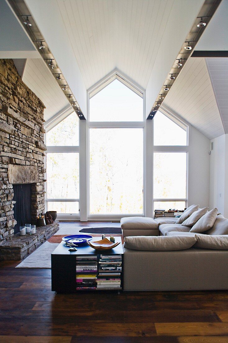Wohnraum mit Sofa und rustikalem offenen Kamin vor raumhohem Giebelfenster