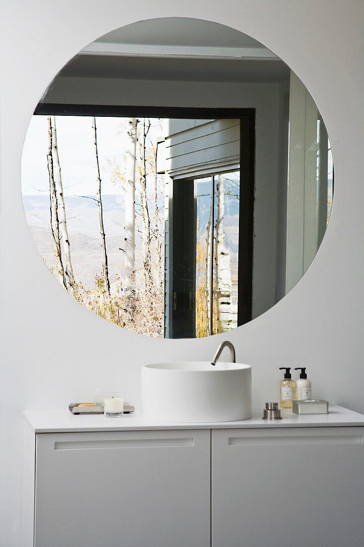 A white designer wash stand with a cupboard underneath and a round wall mirror