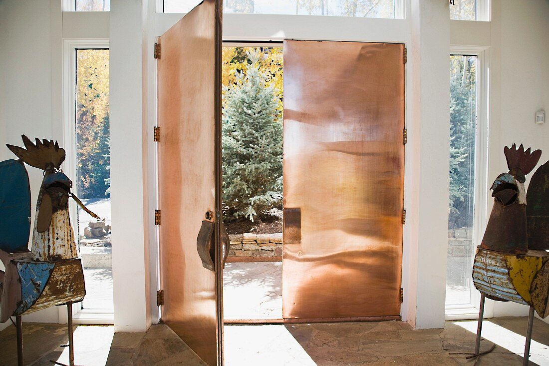 Künstlerische Metallarbeiten neben offener Eingangstür aus Kupfermetall und Blick in Garten