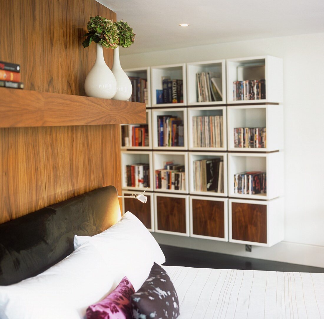 A bed with an upholstered headboard and a contemporary shelf with cubic modules on the wall