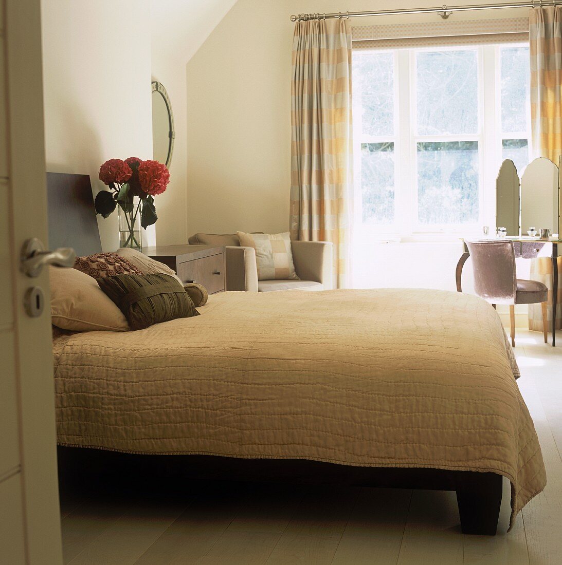 A view through an open door onto a double bed with a white quilt and a dressing table in the corner