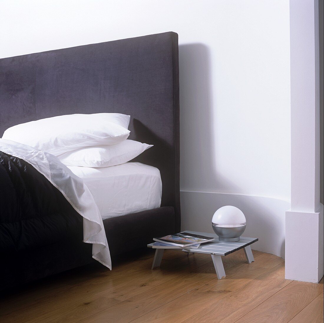 A stack of white cushions on a double bed with a black upholstered headboard and a mini bedside table