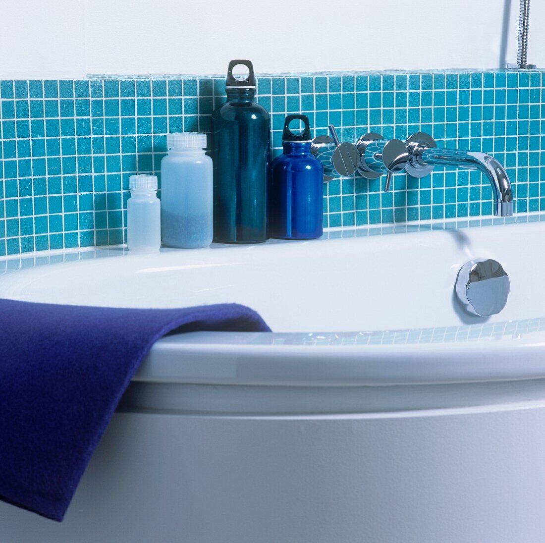 Ausschnitt einer Badewanne mit blauen Behältern vor blauen Fliesen an Wand