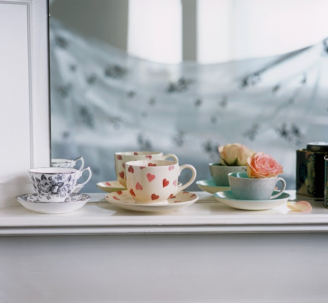 A collection of vintage cups on a shelf in front of a mirror
