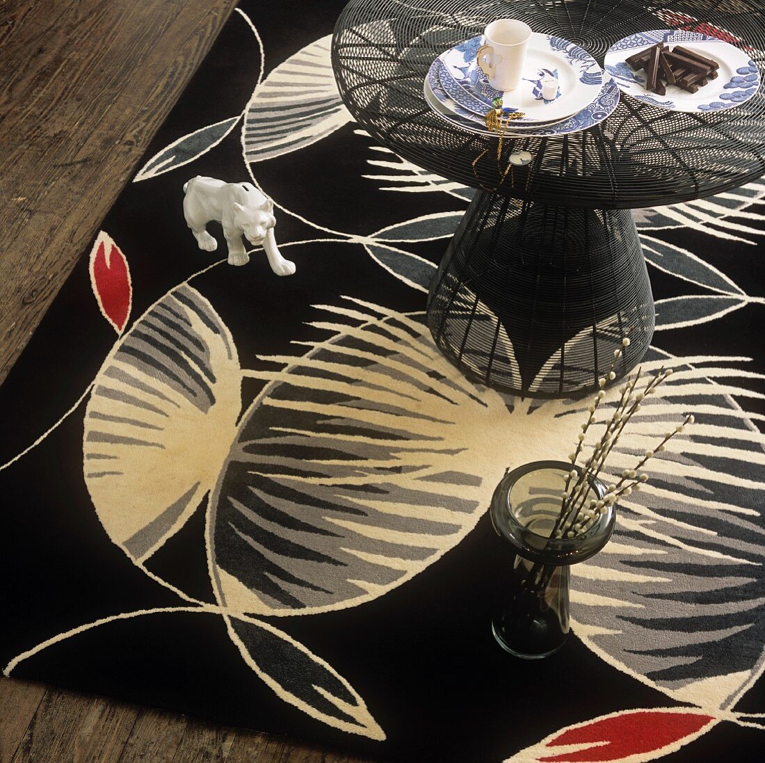 Kaffeetisch, Bodenvase und Tierfigur auf einem gross gemusterten schwarzen Teppich