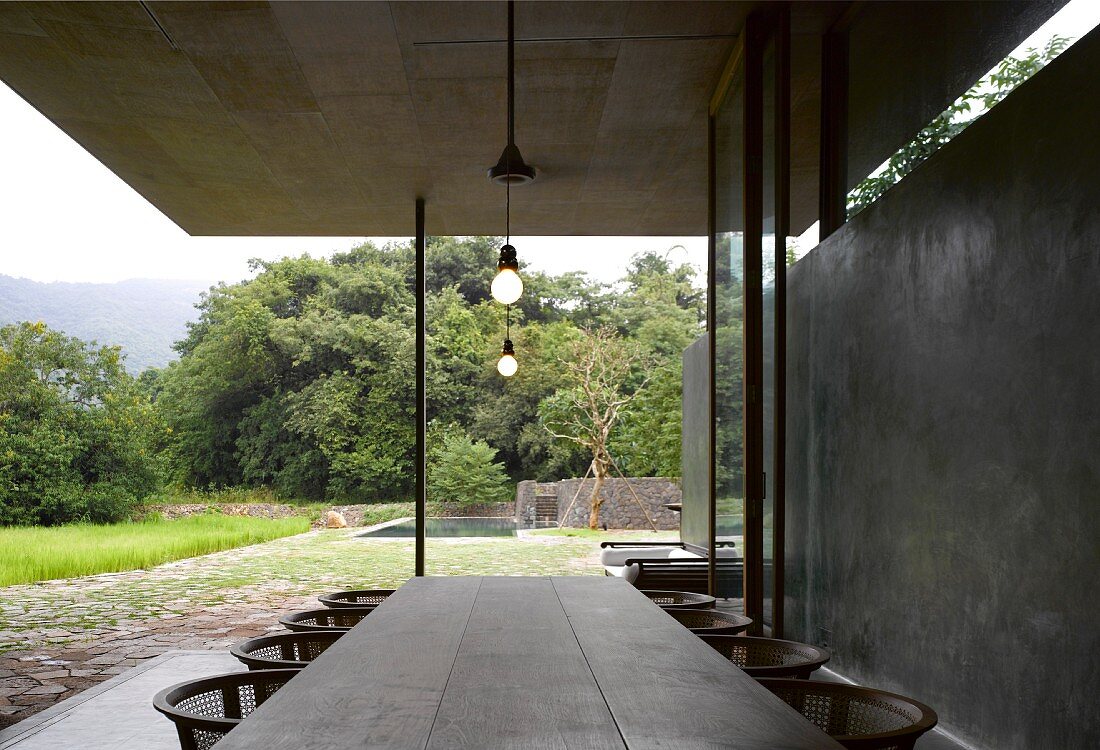 Rustic table on veranda of contemporary house with concrete wall and view into garden