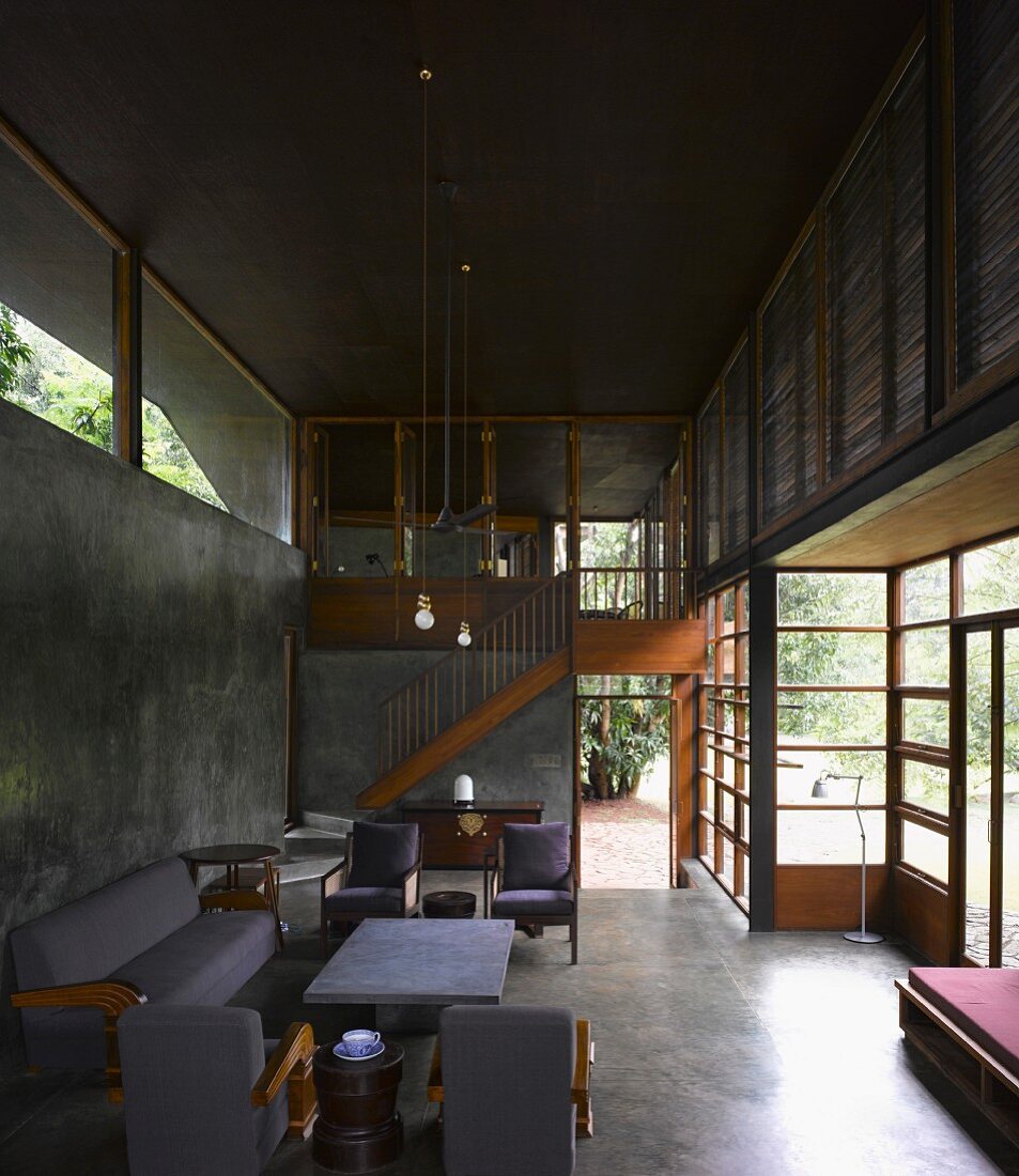 Graue Sofagarnitur im zeitgenössischen offenen Wohnraum aus Beton und Holzglasfassade mit Gartenblick