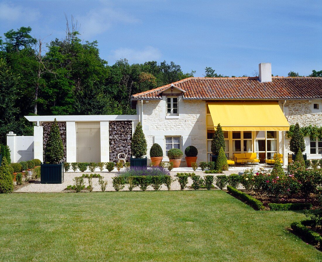 Elegantes Landhaus mit gelber Markise über Terrassenplatz und gepflegtem Garten