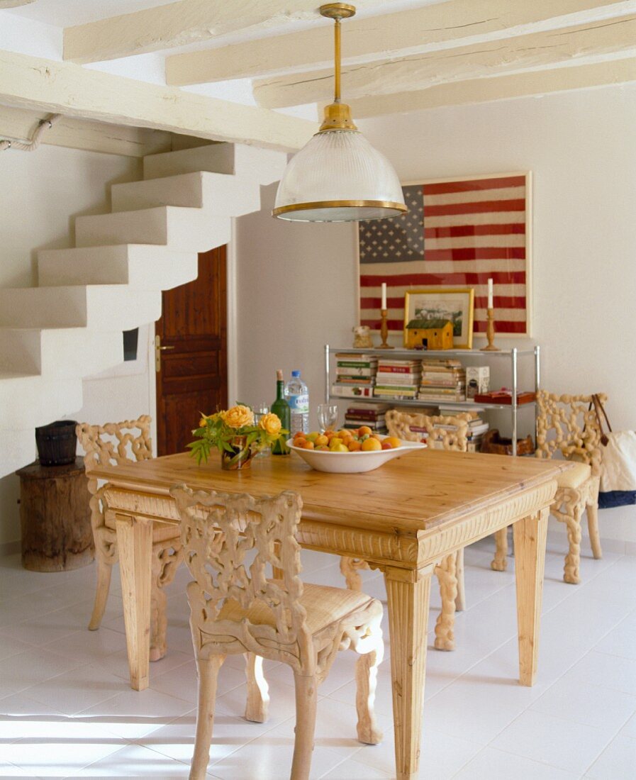 Carved wooden chairs and table in a rustic white dining room with open stairway