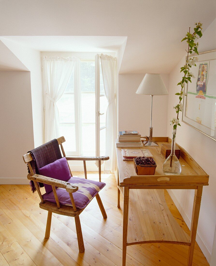 A rustic wooden armchair in front of a simple desk in an attic room