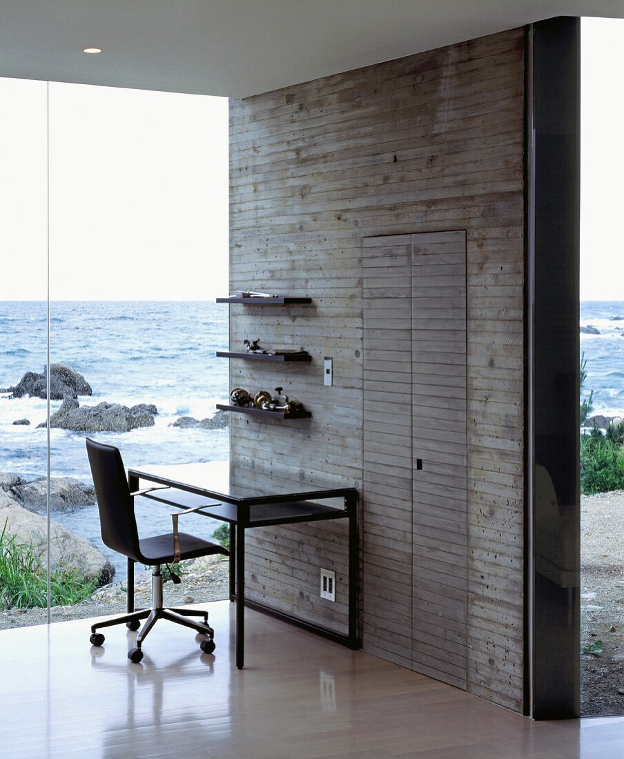 Puristische Arbeitsecke vor Betonwand und Glasfassade mit Blick auf das Meer