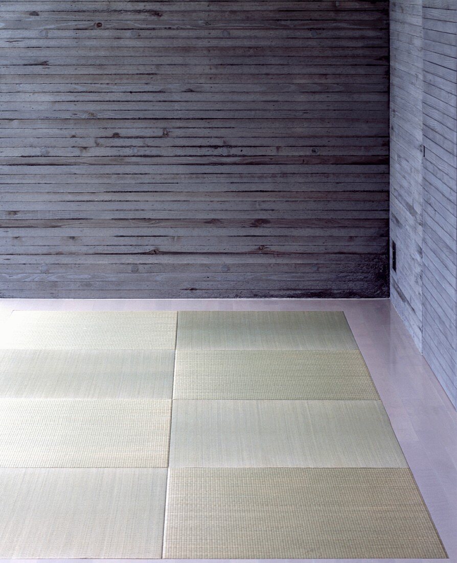 A corner of a room with exposed concrete walls and tatami mats on the floor