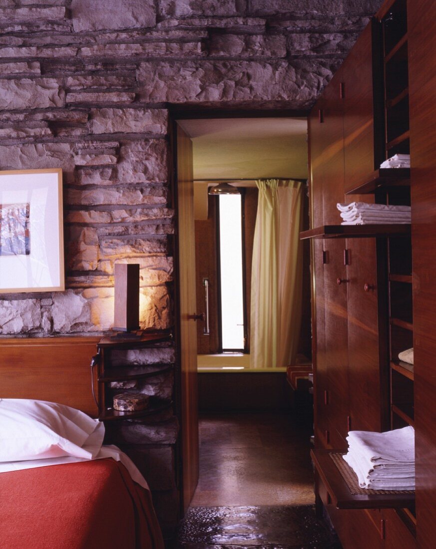 A natural stone wall in a bedroom with a view through an open door into a bathroom