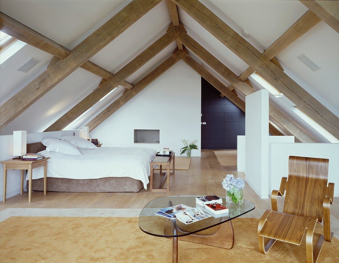 A bedroom in a converted, open-plan attic with armchairs and a coffee table from the 1950s