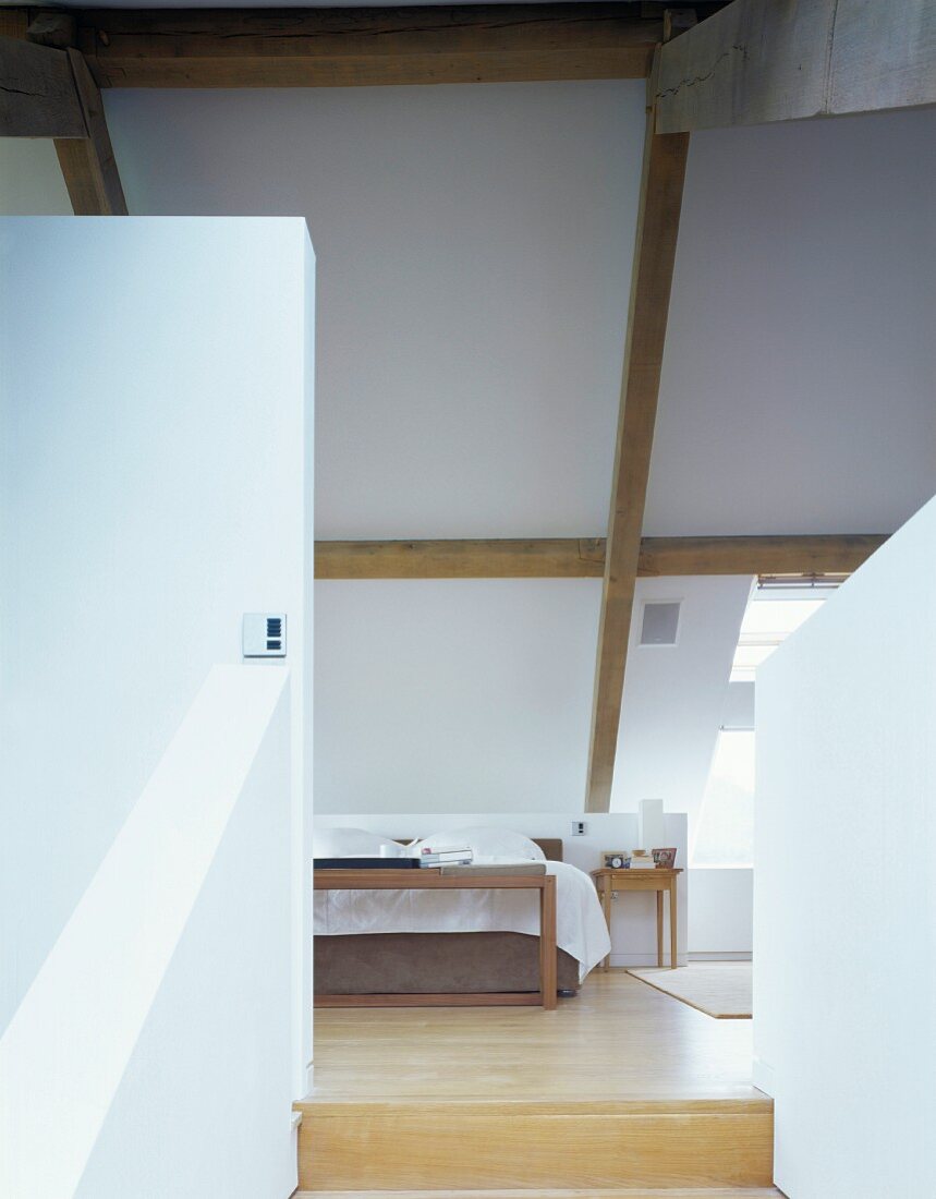 A view between a partition wall and a balustrade wall onto a bed in a converted attic room