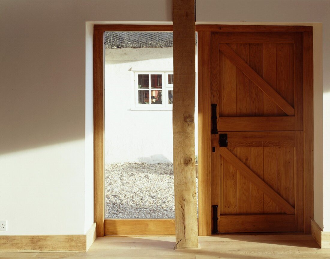 Holzstütze vor raumhohem Fenster und rustikaler Haustür aus Holz