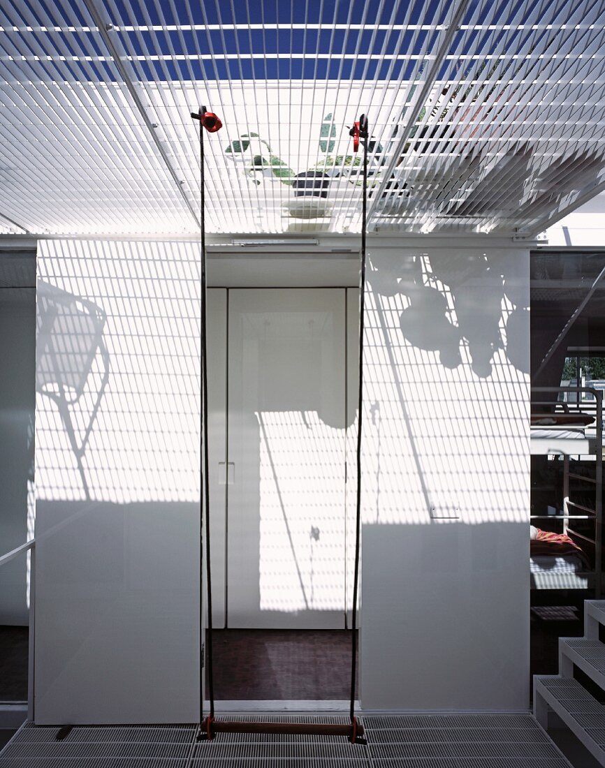 Pattern of light and shade on white wall through wire mesh floor above