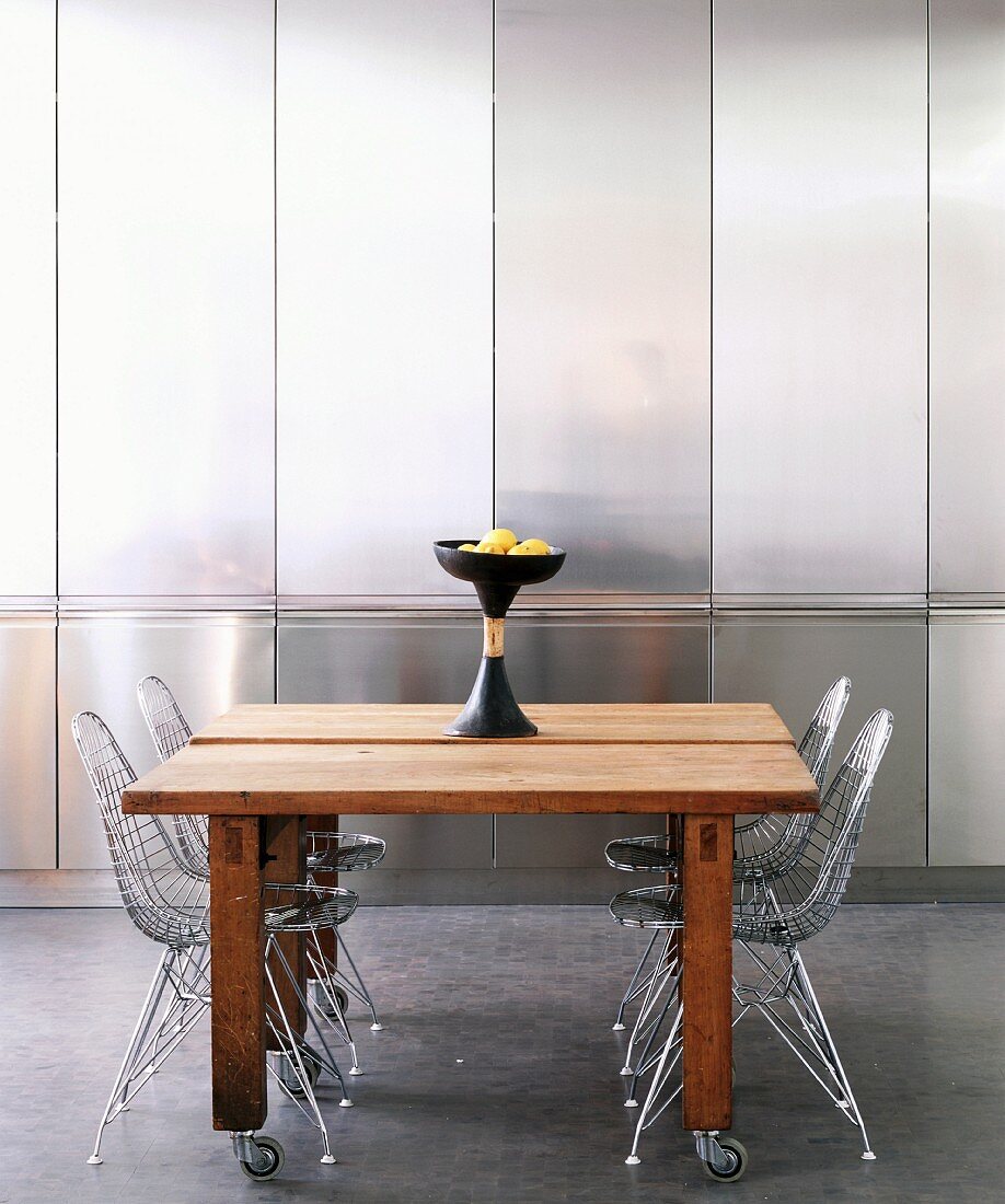 50s-style wire chairs at plain wooden tables on castors in front of stainless steel fitted cupboards