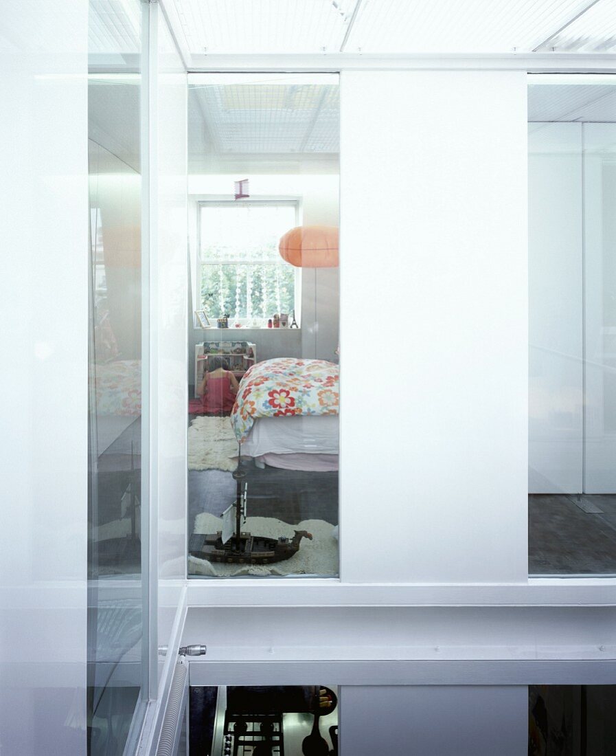 Blick durch spiegelnde Fensterscheibe in Kinderzimmer mit Blumendruck auf Bettwäsche unter orangefarbenem Lampion