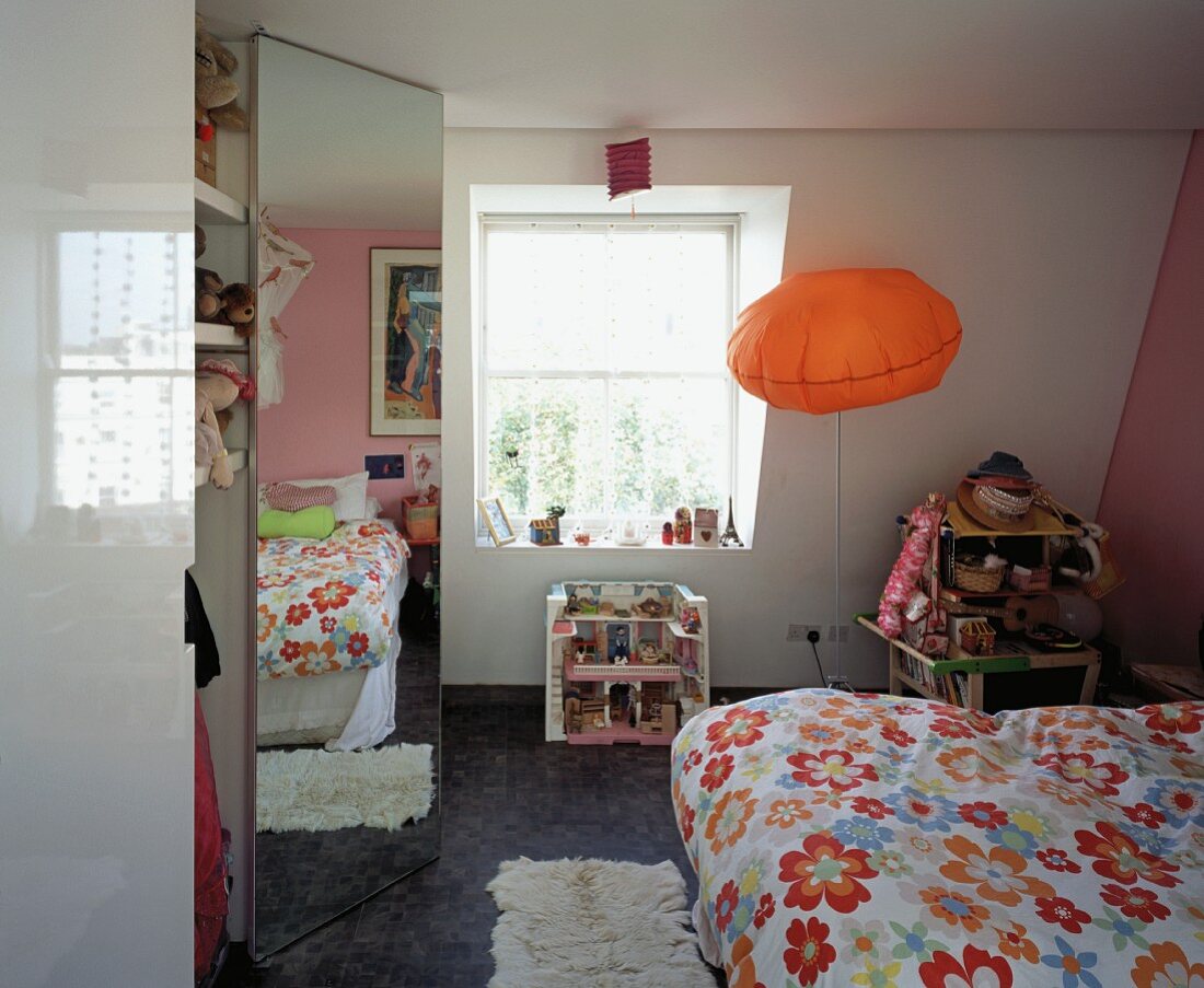 Modernes Kinderzimmer mit orangefarbenem Leuchtkissen und Spiegelung der blumigen Bettwäsche in Einbauschrank