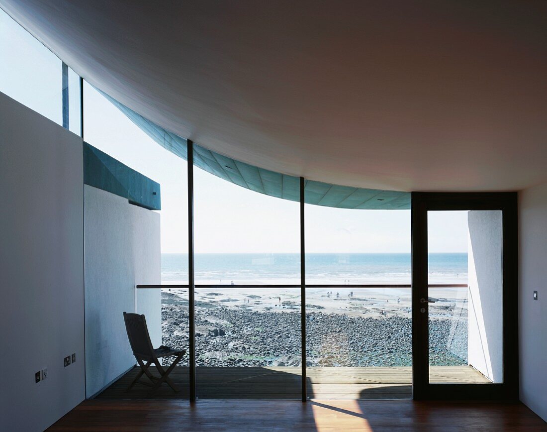 Leerer Wohnraum mit Blick auf angrenzenden Strand durch Glasfassade unter einseitig schwebendem Betondach