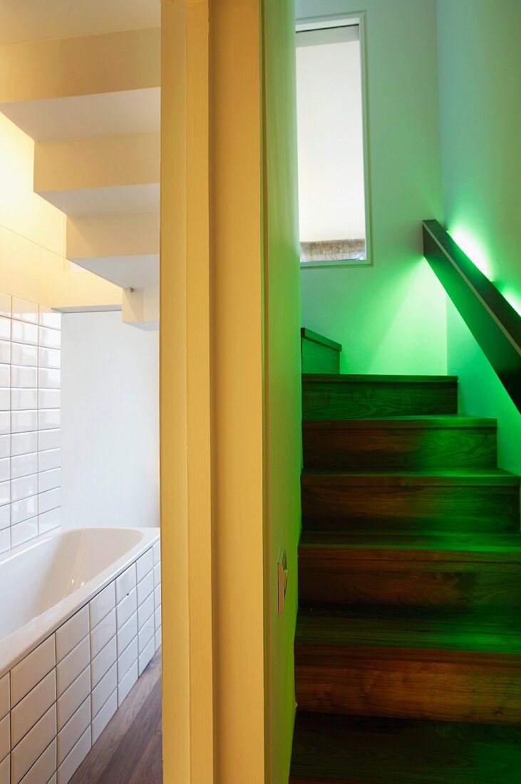In Geländer integrierte, grün schimmernde Beleuchtung an Treppenaufgang neben weiss gefliestem Bad