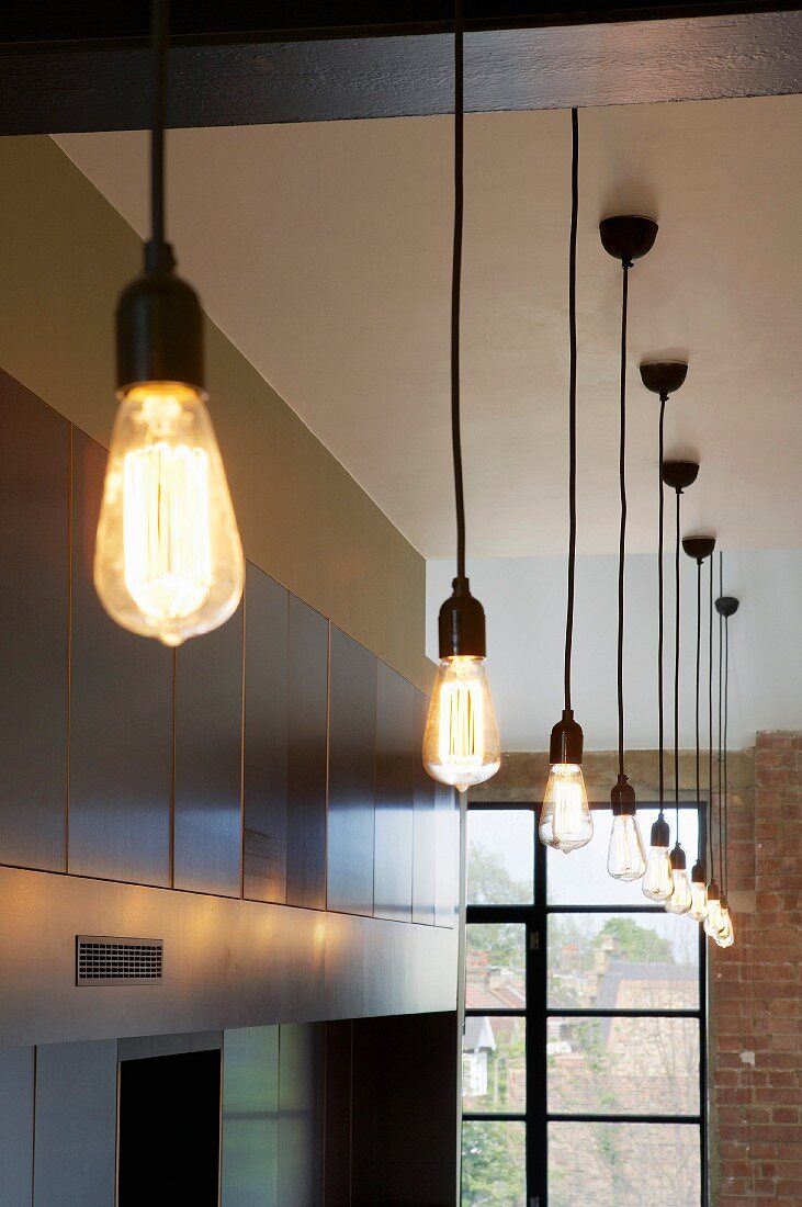 Pendelleuchten mit grossen, tropfenförmigen Glühbirnen in hohem Raum mit traditionellen Fabrikfenstern