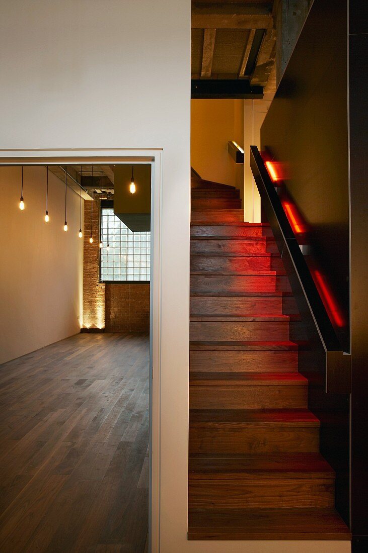 Zentral eingebauter, indirekt farbig beleuchteter Treppenaufgang in Londoner Loft mit Parkett und Industrieverglasung