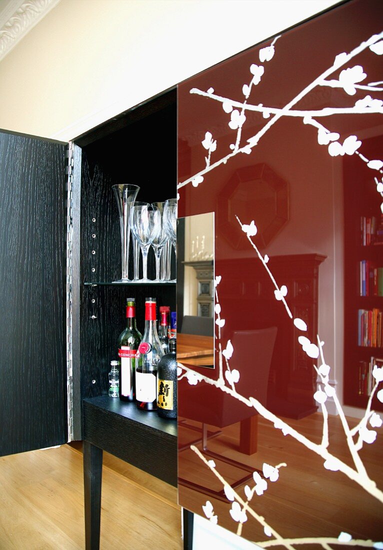 Spiegelung des Wohnzimmers in glänzend rotbrauner Tür mit Blütenzweigmusterung an halb geöffneter Schrank-Bar
