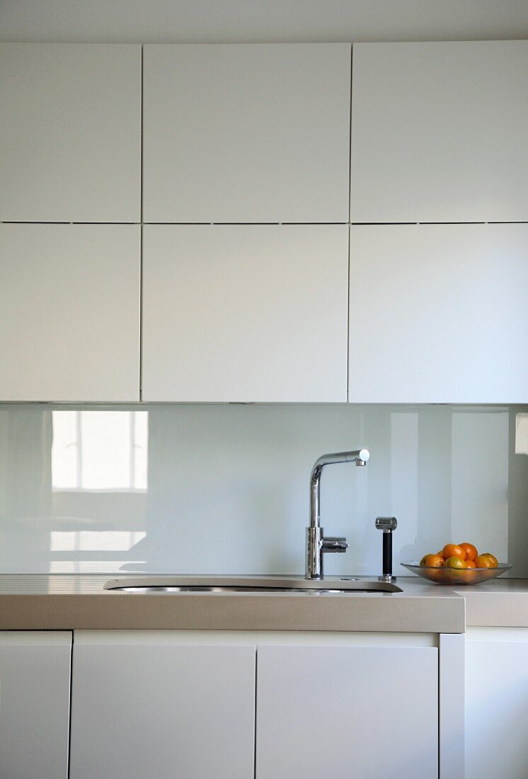 weiße Einbauküche mit glatten Fronten und spiegelndem Spritzschutz aus weißem Glas