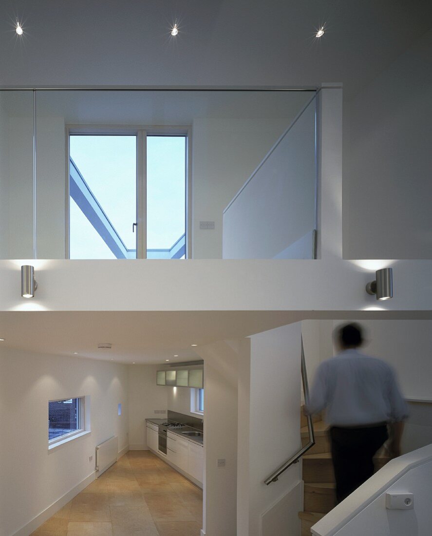 Offenes Wohnhaus mit konisch zulaufender Küche neben Treppenaufgang zu darüberliegender Ebene mit Spiegelung eines Fensters