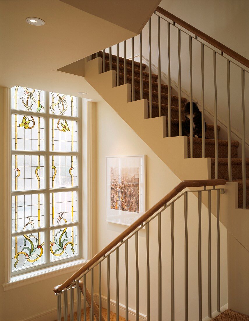 Schlichte, moderne Wohnhaustreppe mit gestufter, weisser Holzwange vor Fenster mit floraler, farbiger Bleiverglasung