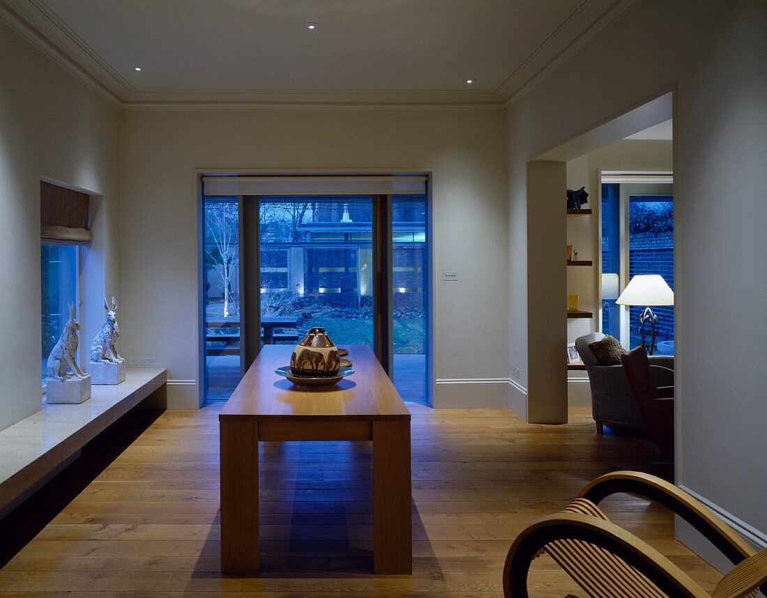 Blaue Stunde in offenem Wohn-/Essraum mit massivem Tisch und auffälligem Schaukelstuhl aus Holz