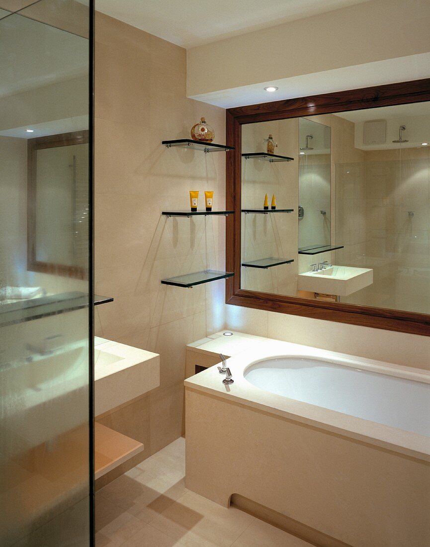 Glass shelves in front of room-width mirror with wooden frame above a stone-clad bathtub