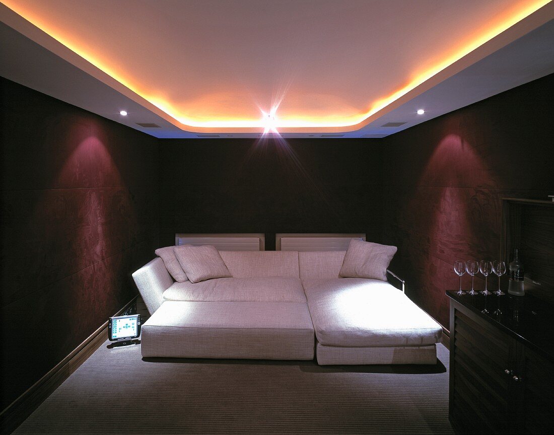 Indirect ceiling lights above wide sofa bed and bar with wine glasses in bordeaux-coloured bedroom