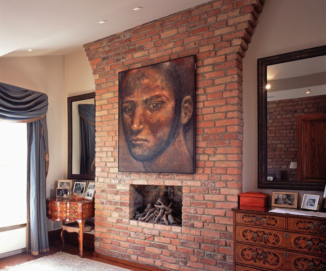 Antique chests of drawers and mirrors on both sides of brick-clad chimney breast with large portrait