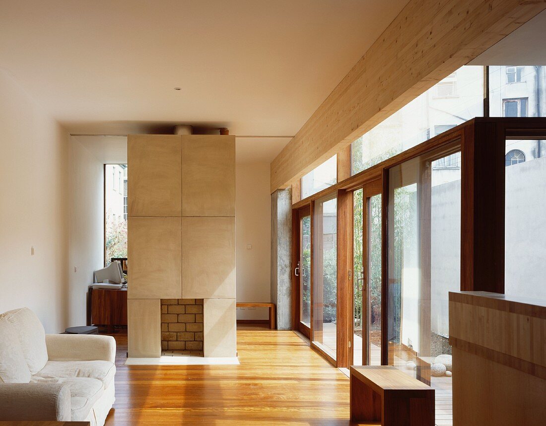 Sofa vor freistehendem gemauerten Kamin im modernen Wohnraum mit Parkettboden und raumhohen Terrassenfenstern