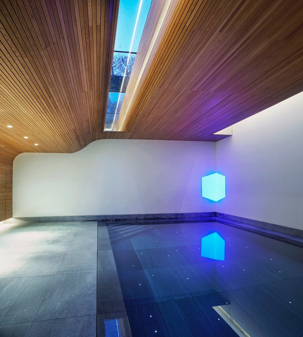 Swimming pool in modern house with partially wood-panelled walls and ceiling with skylight
