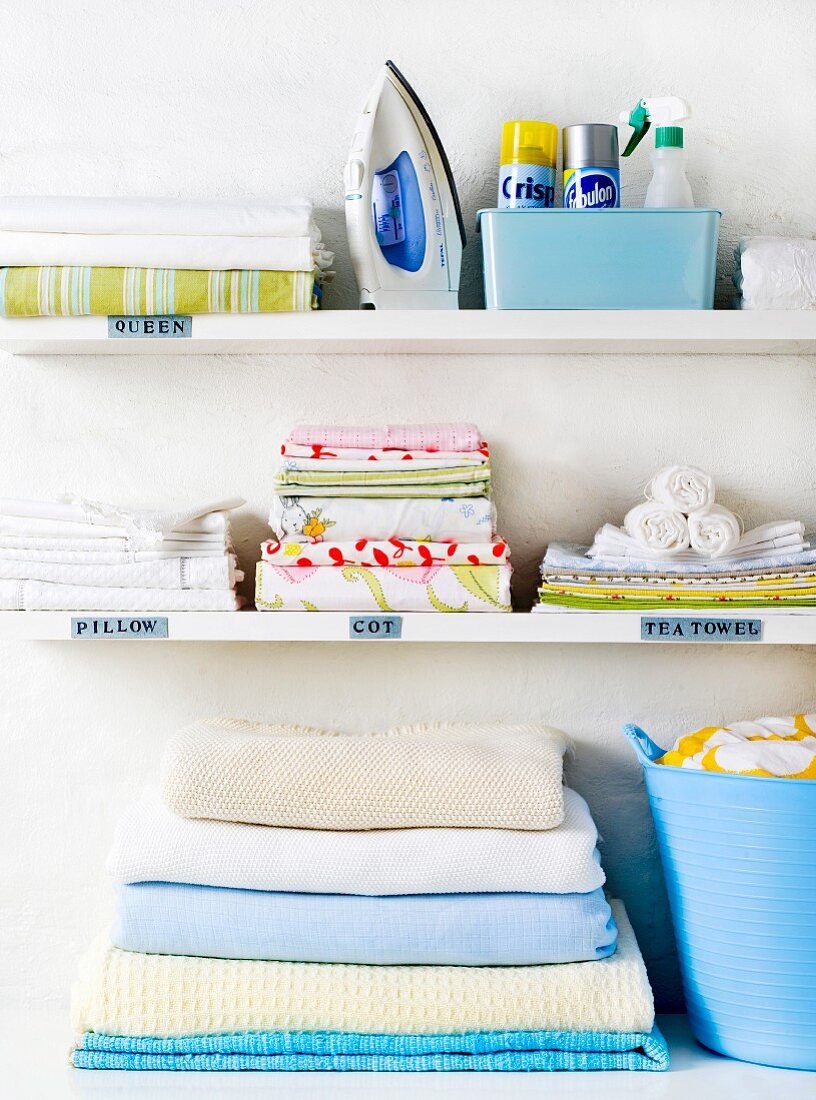 White shelves with ironed washing, iron and cleaning products
