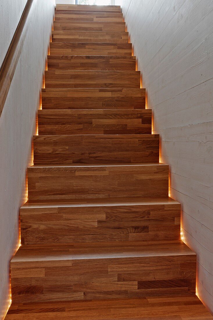 Hinterleuchtete Treppe aus Holz im schmalen Treppenhaus