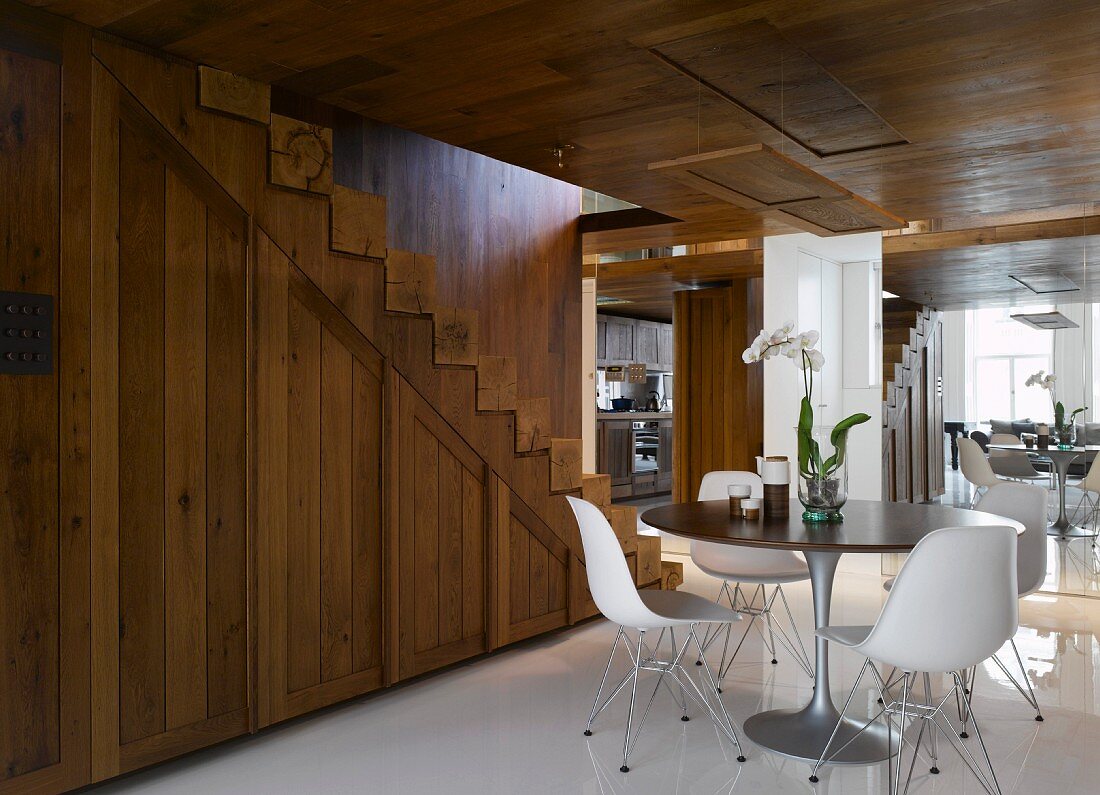 Esstisch mit weissen Schalenstühlen aus Bauhauszeit vor rustikal moderner Holztreppe im offenen Vorraum