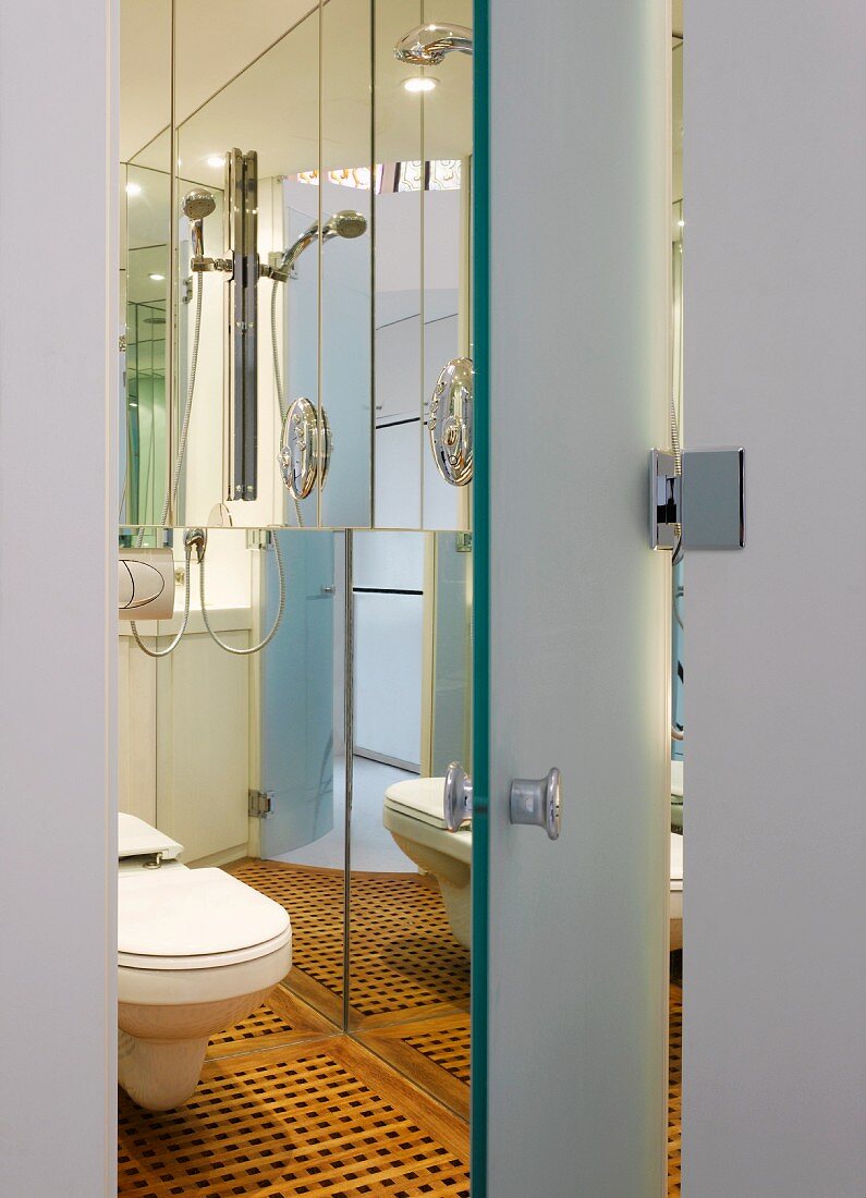 View through open door into modern bathroom with toilet and inlaid wooden floor